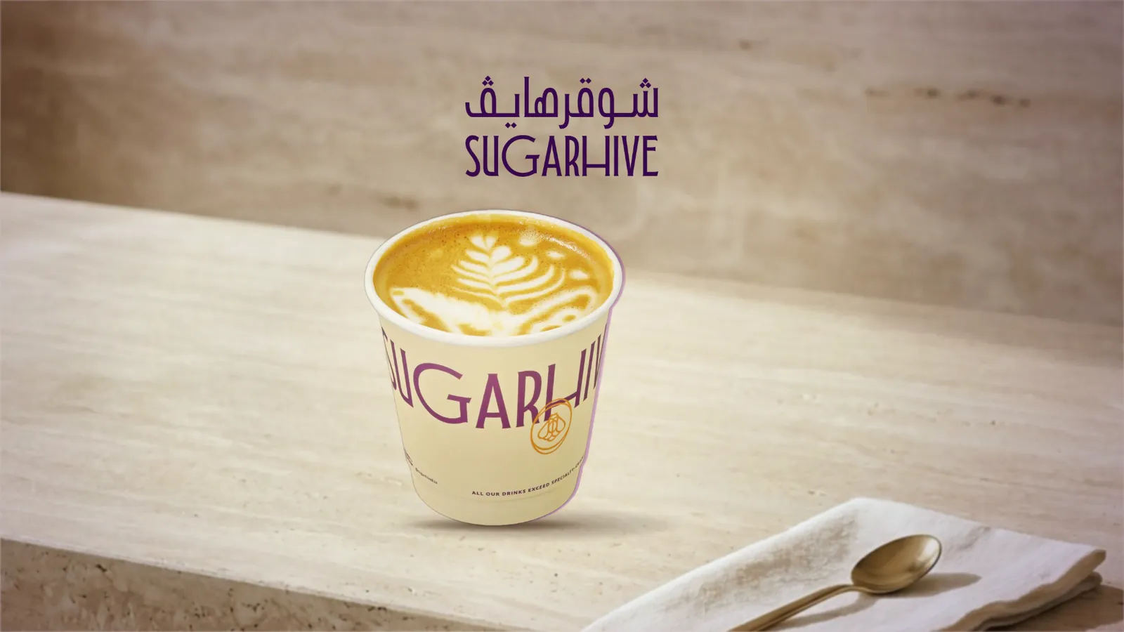 A Sugarhive Spanish latte in its cup on a travertine counter in warm light, the Sugarhive logo above